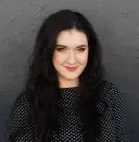 Carrie Buchholz-Powers smiling in front of a dark gray background
