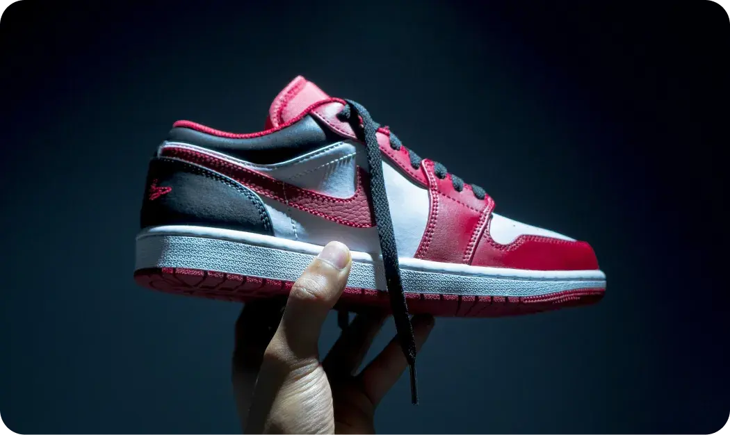 Hand Holding Red And White Sneaker In Dramatic Lighting